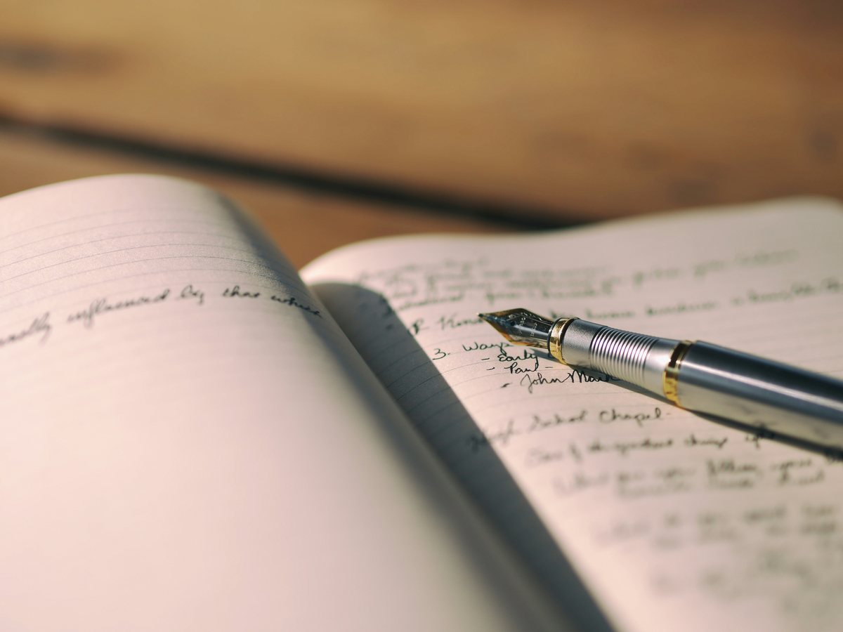 A fountain pen resting on an open handwritten notebook