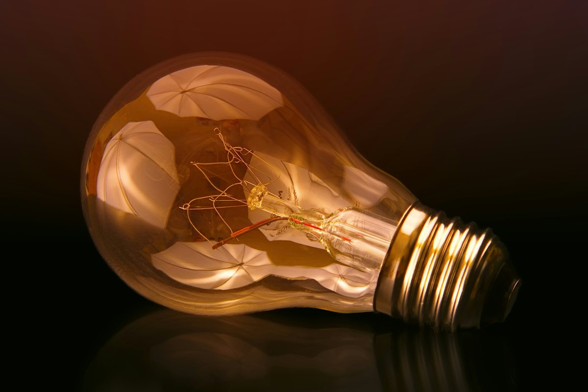A lit filament bulb resting on a dark reflective surface