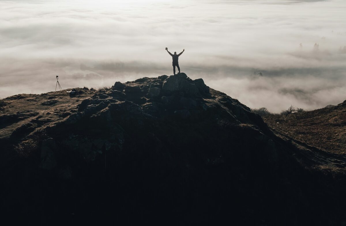 Silhouette with arms raised on mountain summit above clouds