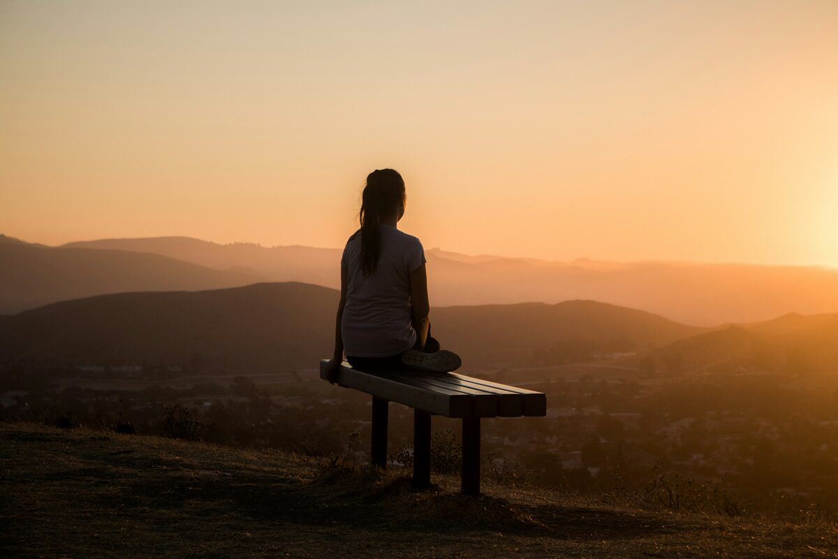 Person sitting on bench at sunset overlooking mountains