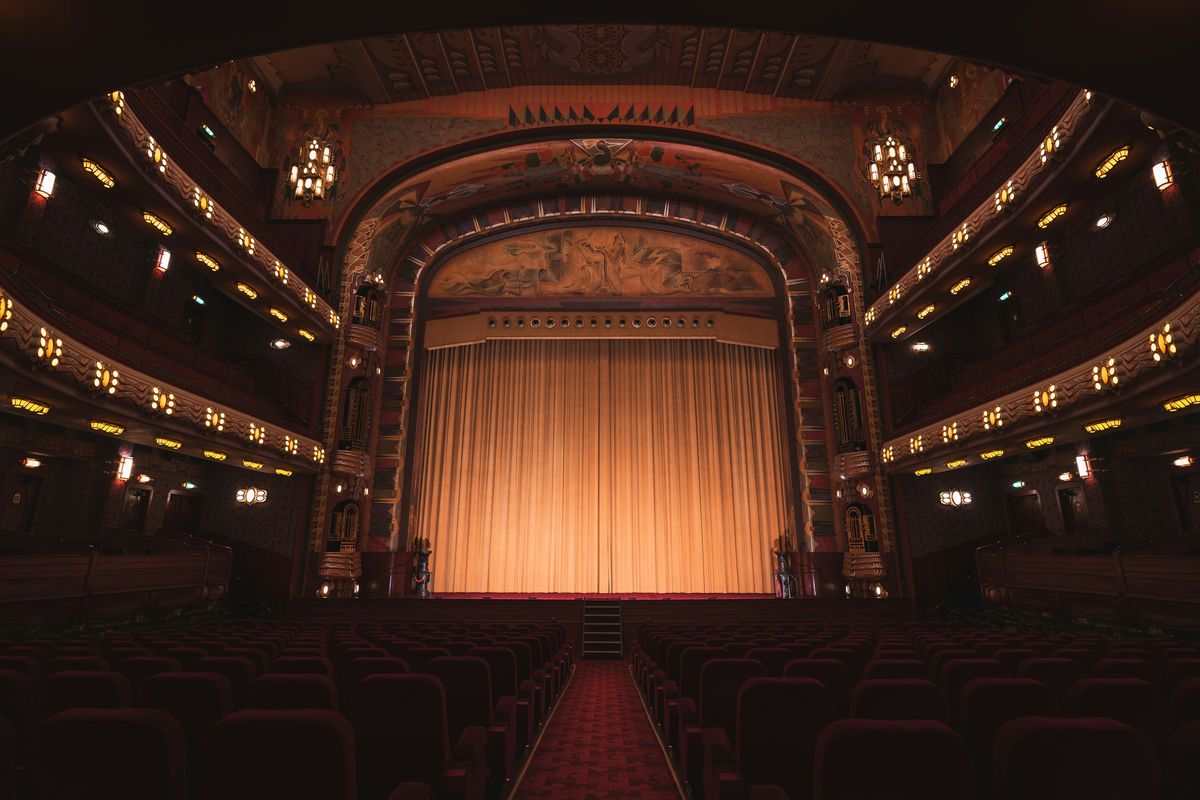 An empty theatre auditorium seen from the aisle, curtain lit on stage