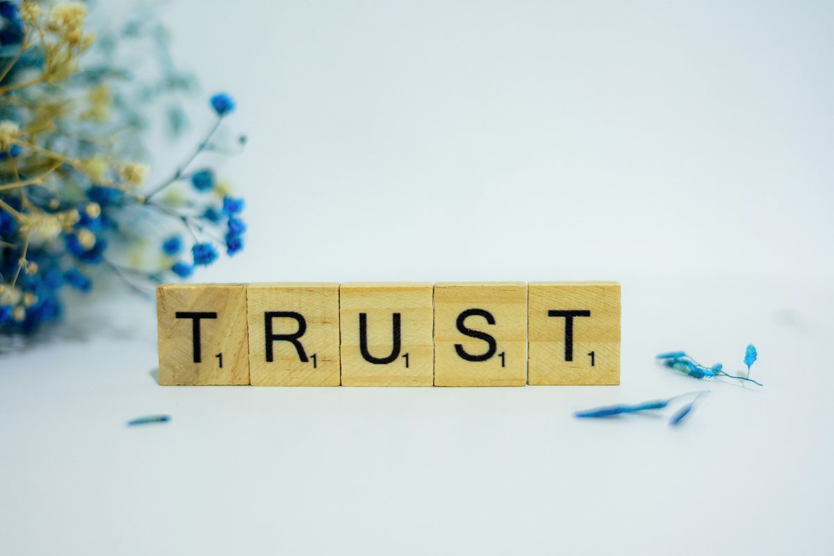 Wooden letter tiles spelling the word trust, beside dried flowers